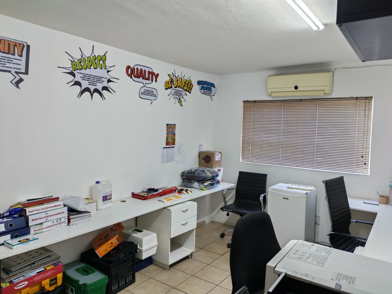 Functional industrial office space featuring built-in desk cabinetry, tiled flooring, wall-mounted air conditioning, and window blinds for light control.