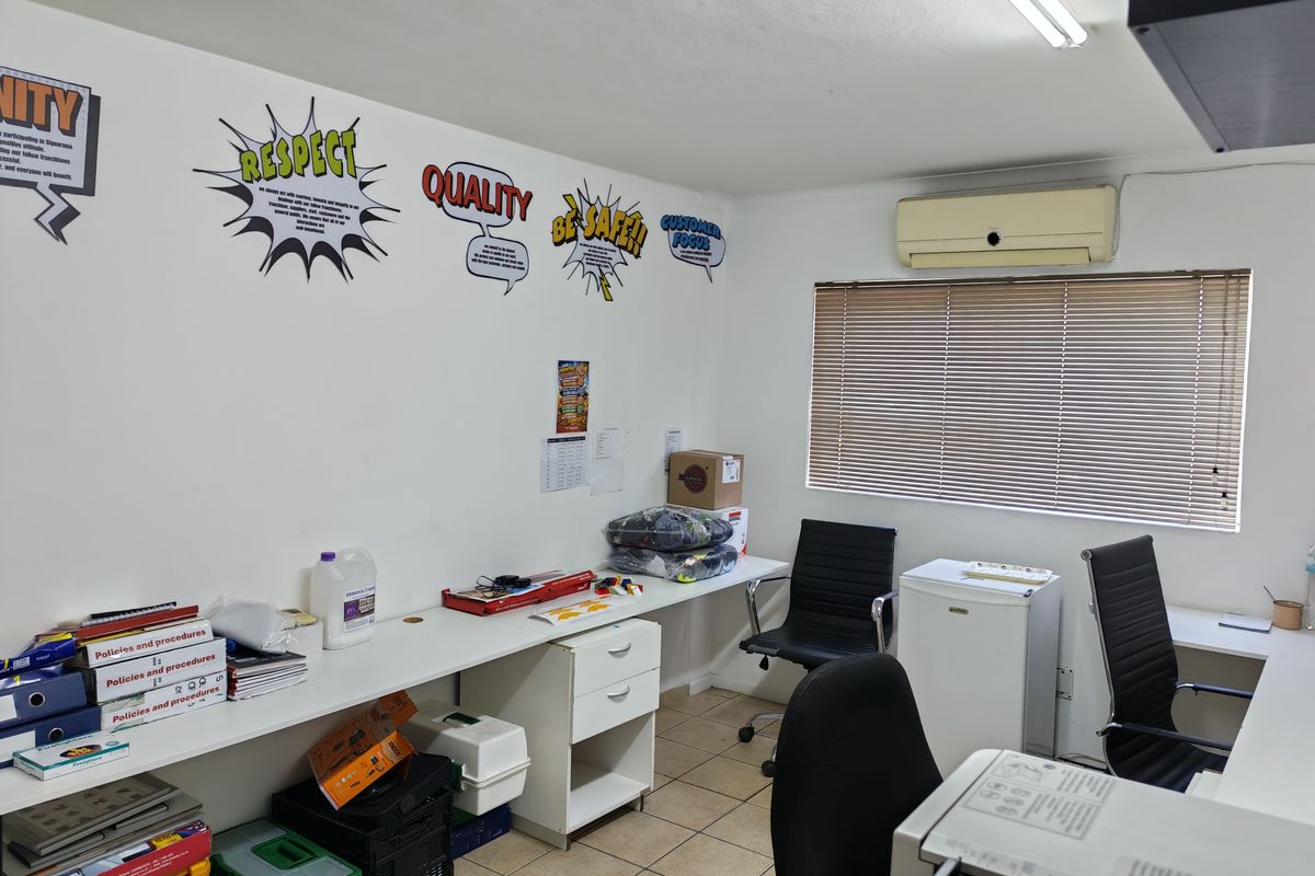 Functional industrial office space featuring built-in desk cabinetry, tiled flooring, wall-mounted air conditioning, and window blinds for light control.