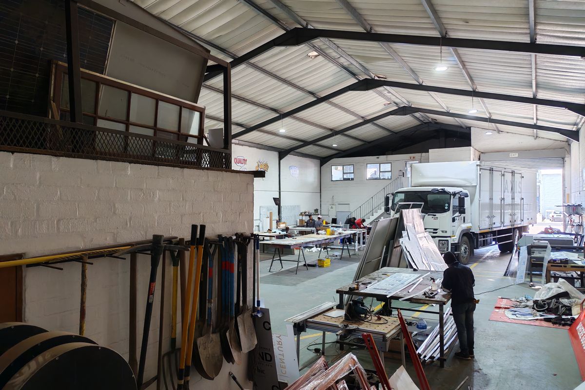 Spacious industrial warehouse featuring high ceilings with exposed steel trusses, concrete flooring, a mezzanine level, and a large roller shutter door for vehicle access.