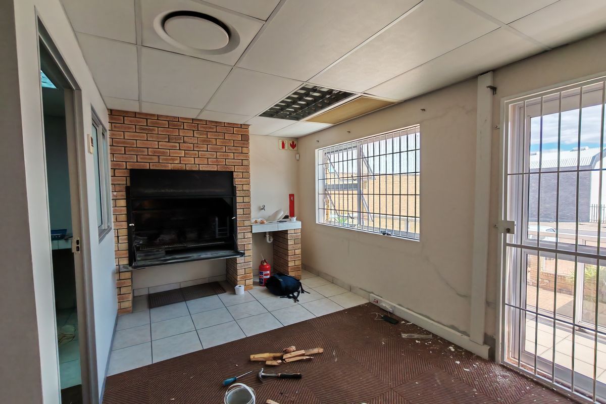 Industrial entertainment area featuring a built-in brick braai, tiled flooring, security bars on windows, and a suspended ceiling system.
