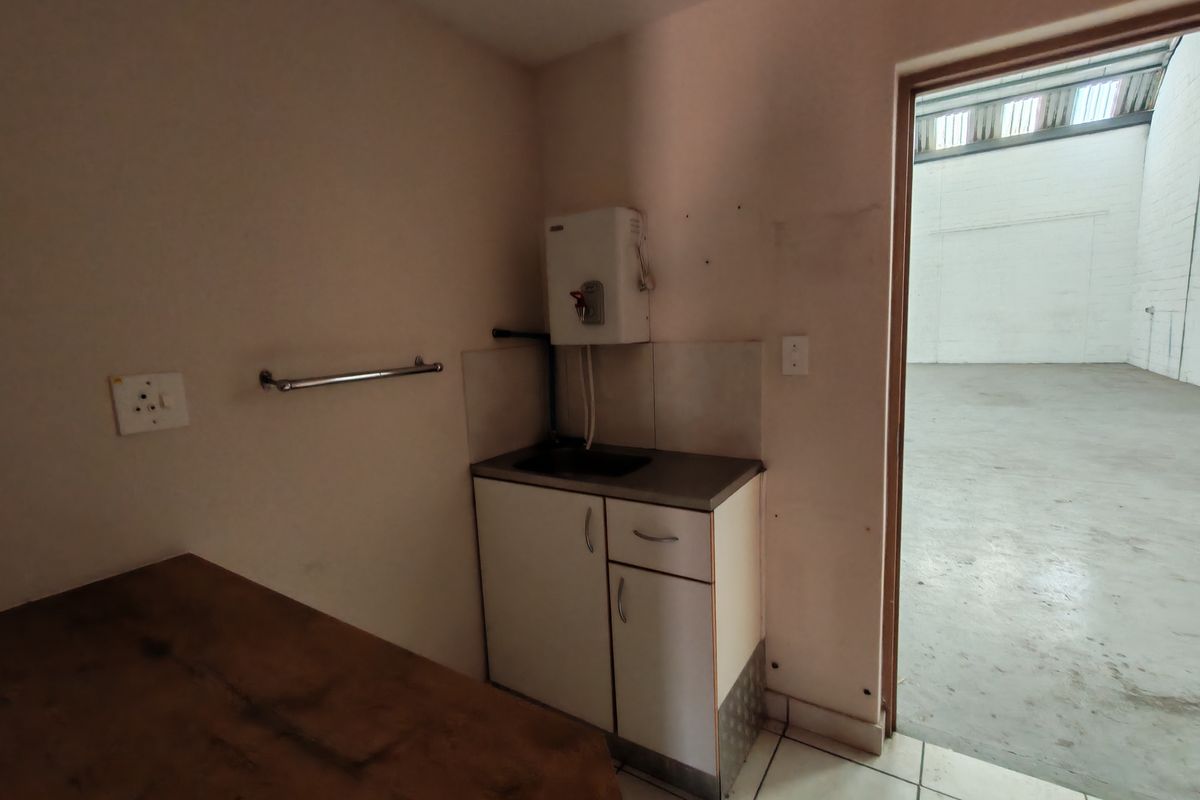 A functional kitchenette area featuring a small sink, built-in cabinetry, and a wall-mounted water heater, adjacent to a large industrial warehouse space.