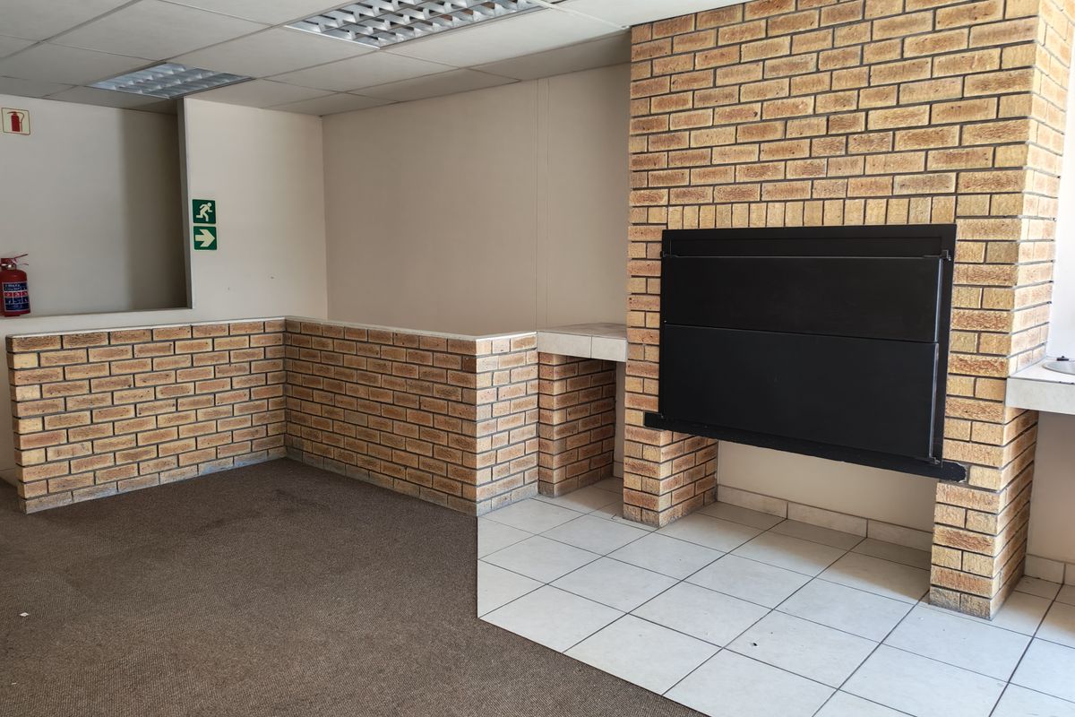 Spacious industrial interior featuring a built-in brick fireplace, tiled and carpeted flooring, and recessed ceiling lighting.