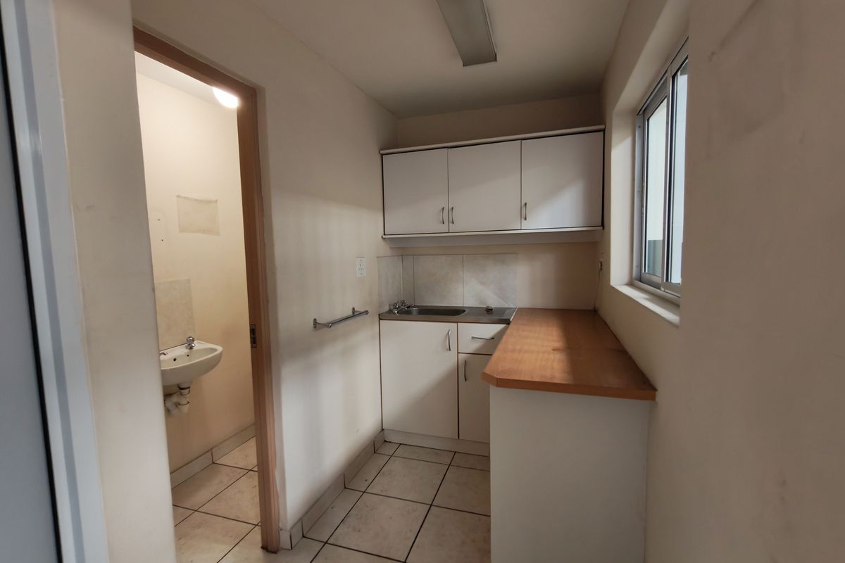 A functional kitchenette area featuring built-in cabinetry, a sink, and tiled flooring, with an adjacent small washroom facility.