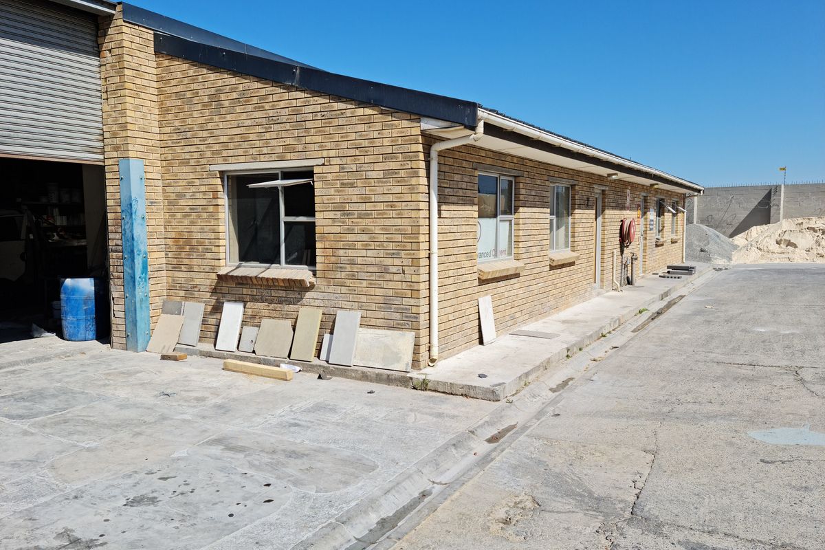 Exterior view of an industrial brick building featuring a roller shutter door, concrete apron, and external fire hose reel.