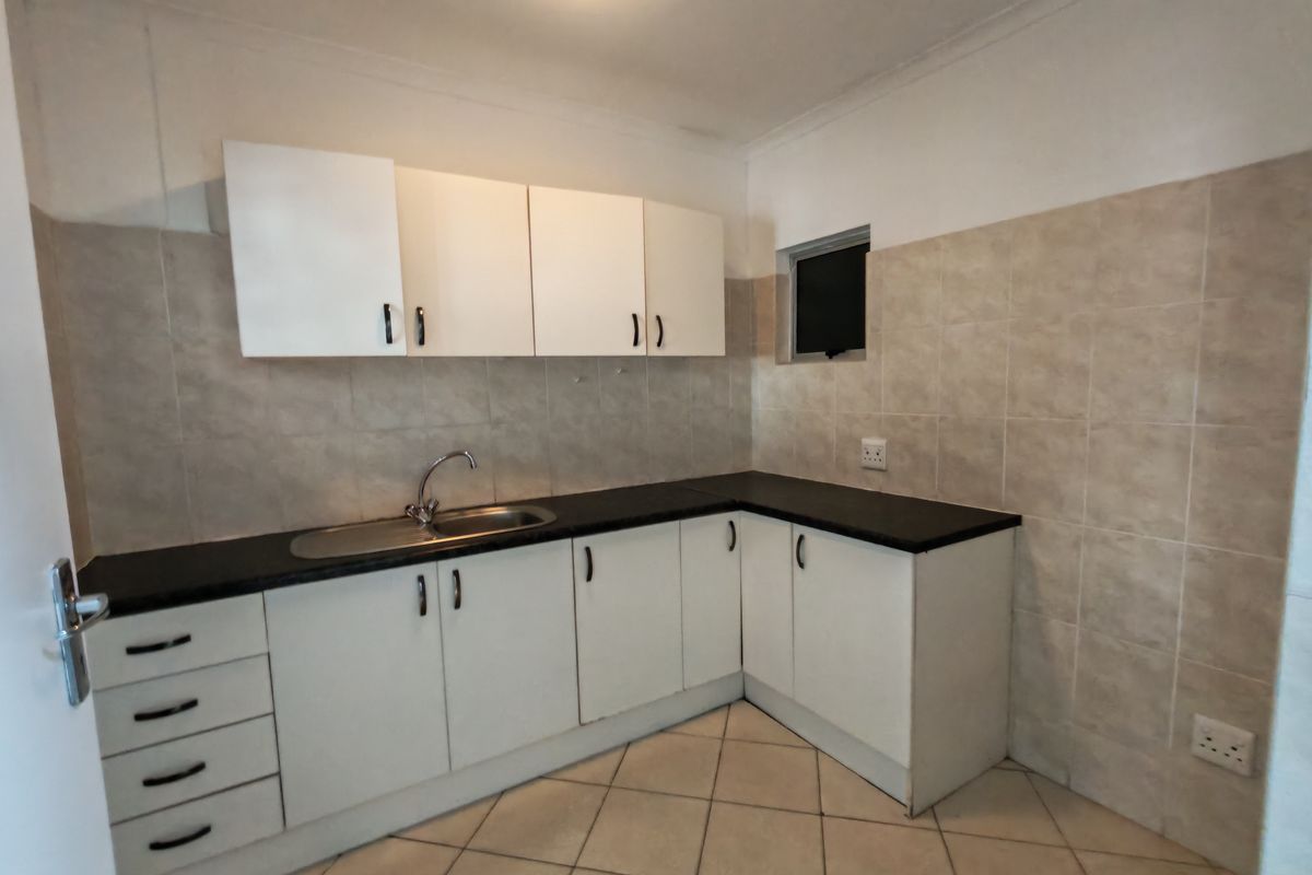 Compact kitchen featuring white cabinetry, dark laminate countertops, stainless steel sink, and neutral wall tiling.