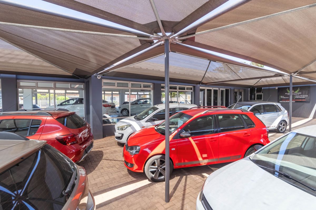 Covered outdoor vehicle display area featuring a large shade sail structure and paved flooring, suitable for a commercial car dealership.