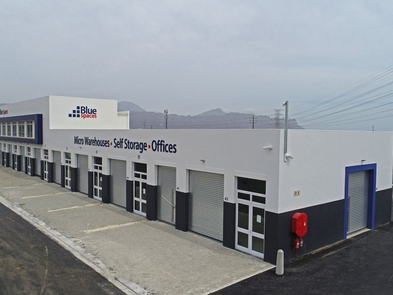 Aerial view of a modern industrial facility featuring multiple micro-warehouse units with roller shutter doors, paved driveway, and clear signage.