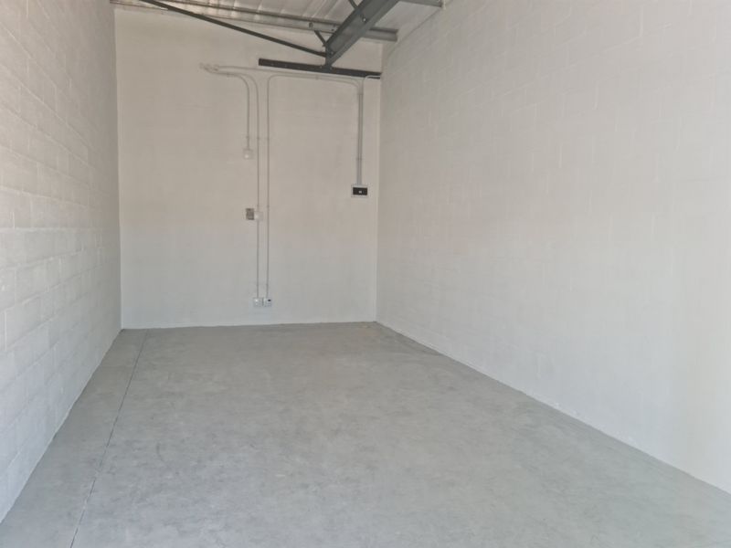 A clean, empty industrial utility space featuring painted concrete block walls, exposed steel roof trusses, and durable concrete flooring.