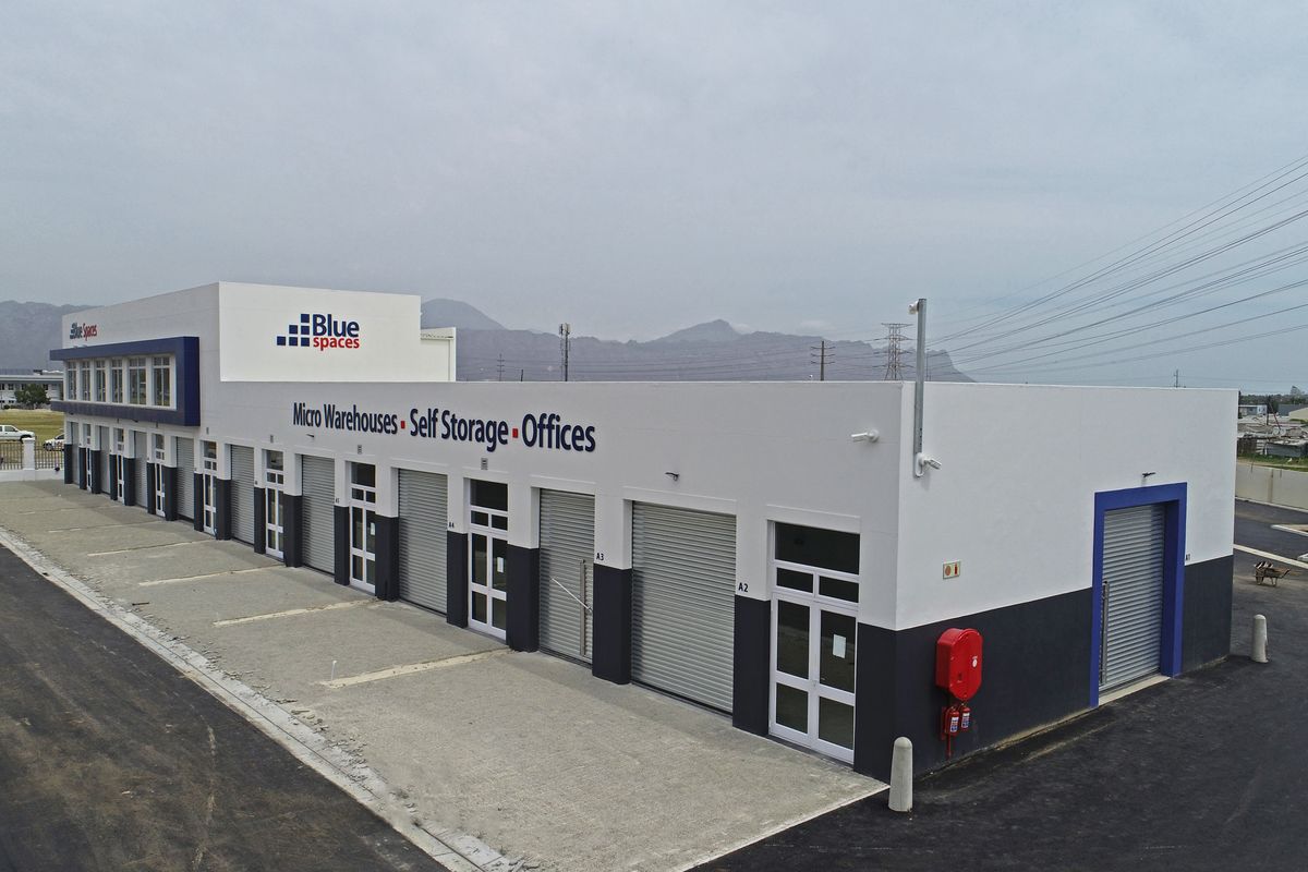 Aerial view of a modern industrial facility featuring multiple micro-warehouse units with roller shutter doors, paved driveway, and clear signage.