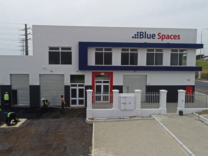 Aerial view of a modern industrial office complex featuring roller shutter doors, paved driveway, and secure perimeter fencing.