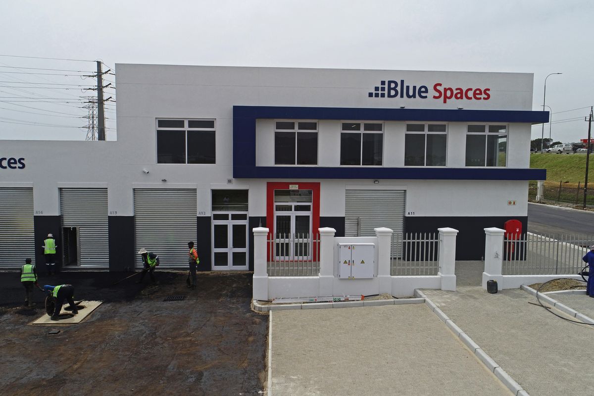 Aerial view of a modern industrial office complex featuring roller shutter doors, paved driveway, and secure perimeter fencing.