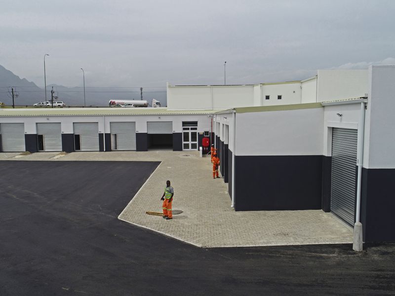 Aerial view of a modern industrial complex featuring multiple roller shutter doors, paved yard space, and clean exterior finishes.
