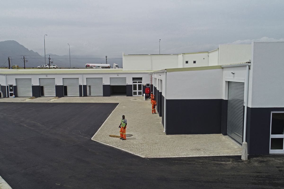 Aerial view of a modern industrial complex featuring multiple roller shutter doors, paved yard space, and clean exterior finishes.