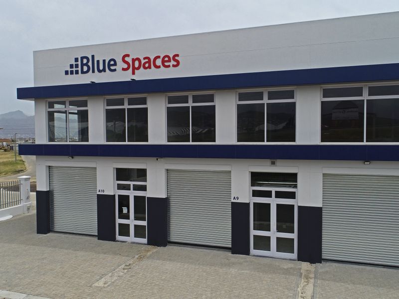 Modern industrial commercial building featuring multiple roller shutter doors, large windows, and a paved forecourt area.