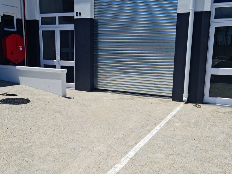 Industrial unit exterior featuring a secure roller shutter door, pedestrian access, and paved frontage with dedicated parking space.