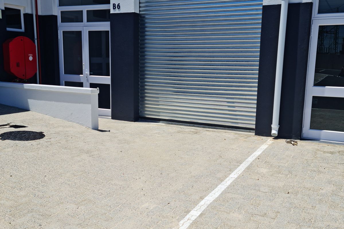 Industrial unit exterior featuring a secure roller shutter door, pedestrian access, and paved frontage with dedicated parking space.