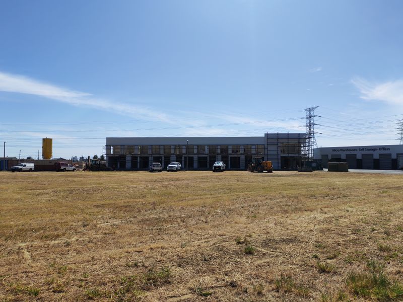 Wide view of an industrial property under construction, featuring a main building with scaffolding and an adjacent self-storage facility on a large open lot.