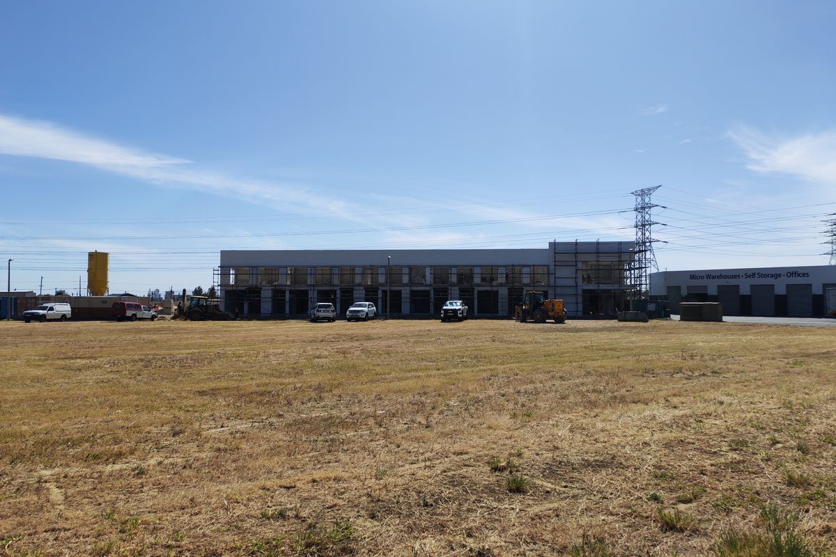 Wide view of an industrial property under construction, featuring a main building with scaffolding and an adjacent self-storage facility on a large open lot.