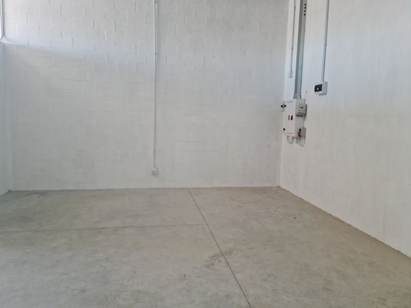A clean, empty industrial utility space featuring painted blockwork walls, polished concrete flooring, and wall-mounted electrical distribution infrastructure.