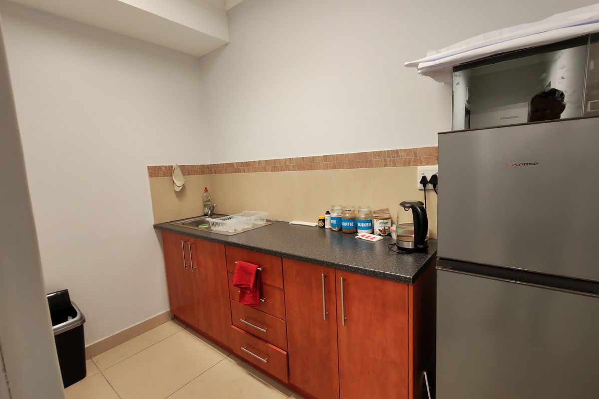 A functional kitchenette area featuring wooden cabinetry, a dark laminate countertop, a stainless steel sink, and tiled splashback.