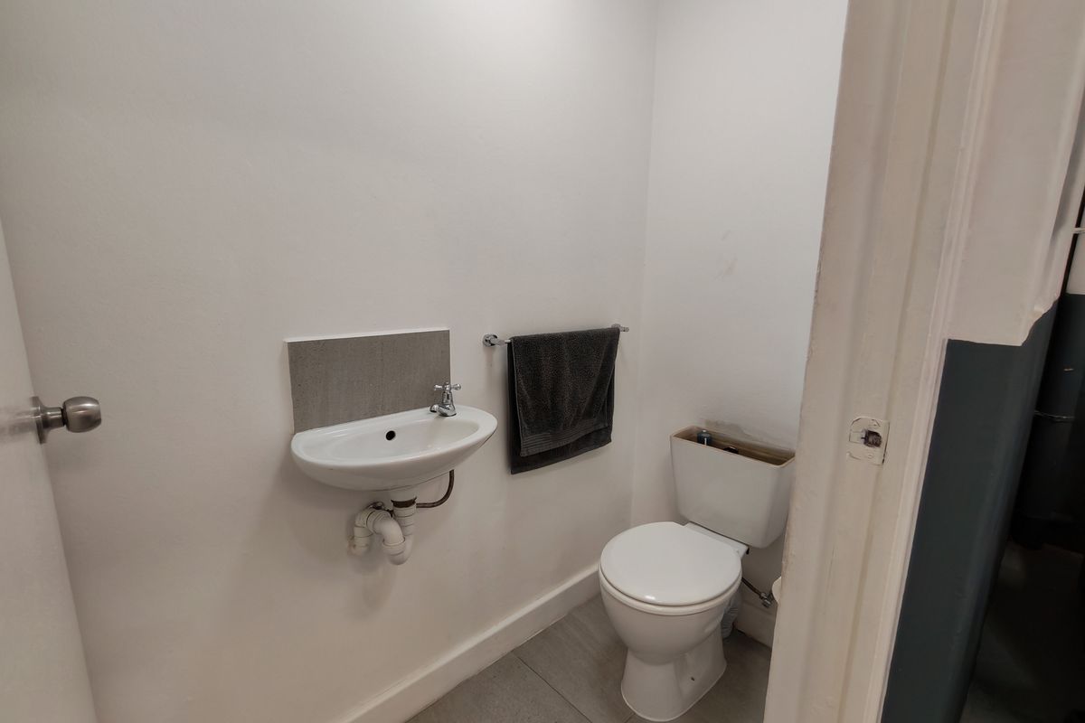 A compact powder room featuring a wall-mounted basin and a standard toilet suite with tiled flooring.