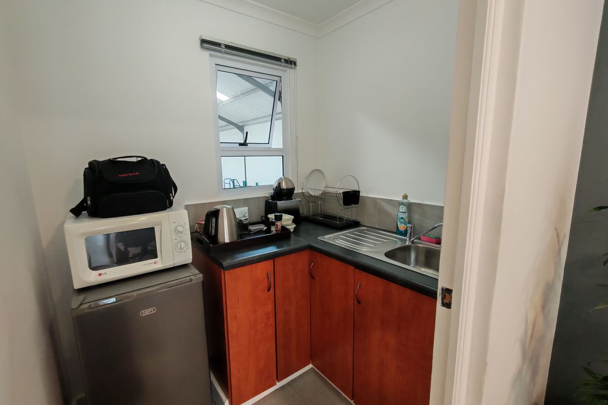 Compact kitchenette area featuring wooden cabinetry, a stainless steel sink, and tiled splashback, suitable for a small office or utility space.