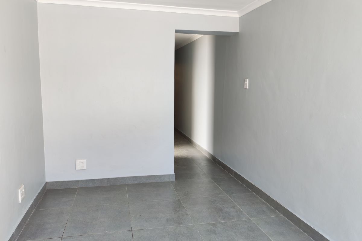 A clean, empty interior space featuring neutral grey walls, tiled flooring, and a doorway leading to a connecting hallway.