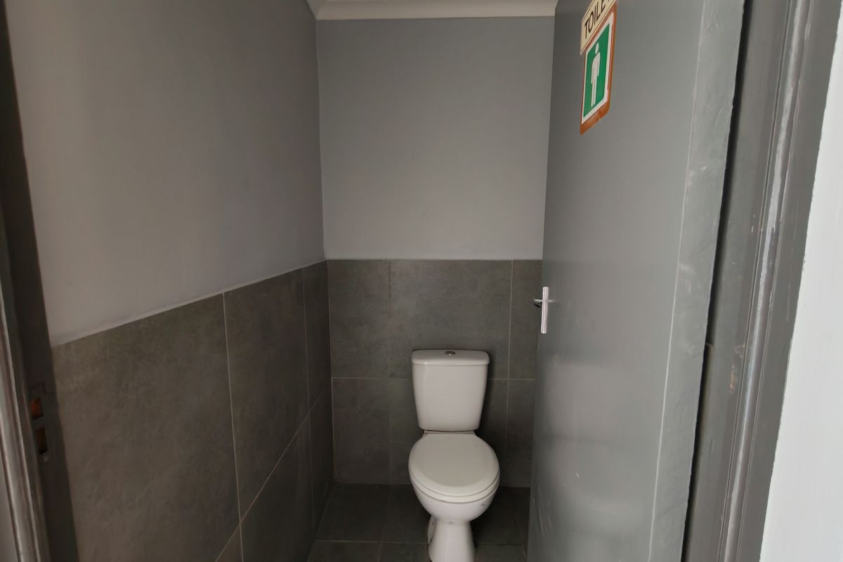 A functional industrial restroom featuring grey wall tiling, a standard white toilet, and a painted door with signage.
