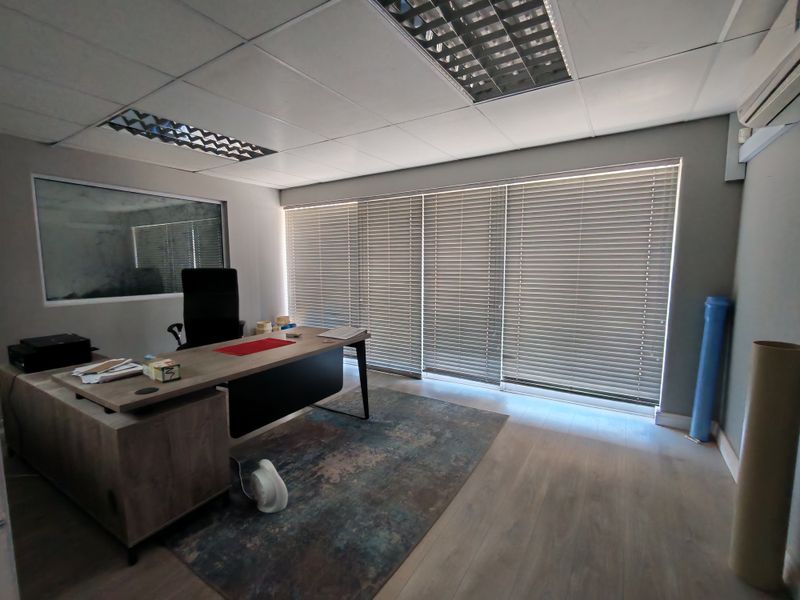 A professional office space featuring laminate flooring, suspended ceilings with recessed lighting, and large windows fitted with venetian blinds.
