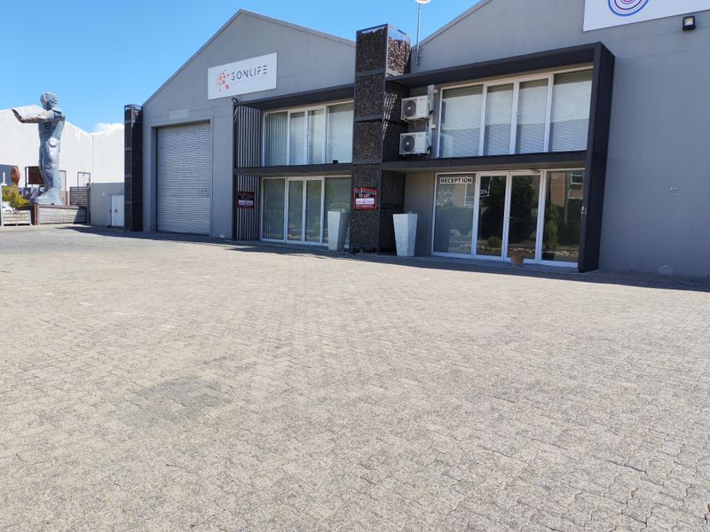 Front elevation of an industrial property featuring a paved driveway, roller shutter door, and a dedicated reception entrance with modern aluminium framing.