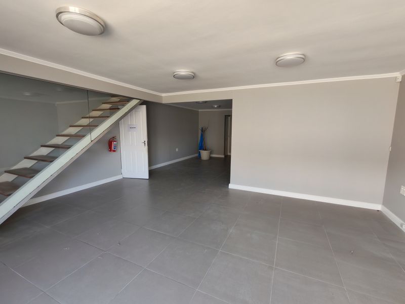 Spacious open-plan industrial area featuring modern grey floor tiles, a contemporary staircase with a glass balustrade, and neutral wall finishes.