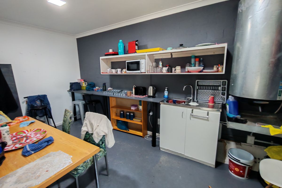 A functional industrial-style kitchenette featuring a stainless steel sink, open shelving, and basic base cabinetry, suitable for a workspace or utility area.