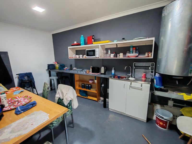 A functional industrial-style kitchenette featuring a stainless steel sink, open shelving, and basic base cabinetry, suitable for a workspace or utility area.