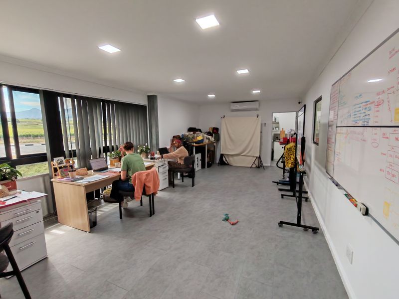 Spacious industrial office area featuring recessed lighting, split-system air conditioning, large windows with vertical blinds, and a wall-mounted whiteboard.