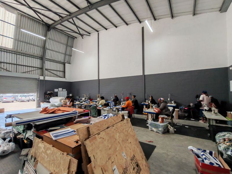 Spacious industrial warehouse unit featuring high ceilings with exposed steel trusses, concrete flooring, and a large roller shutter door for easy access.