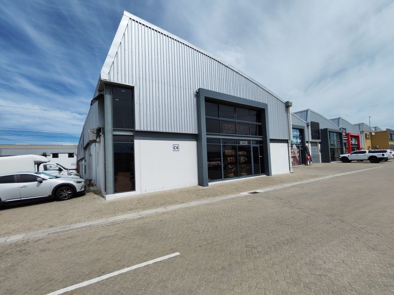 Modern industrial unit featuring corrugated metal cladding, large glass storefront, and paved exterior access in a well-maintained commercial complex.
