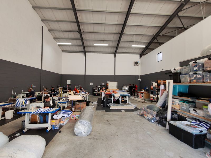 Spacious industrial utility area featuring high ceilings with exposed steel trusses, concrete flooring, and functional lighting, currently utilized as a production workspace.