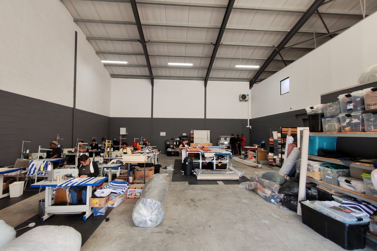 Spacious industrial utility area featuring high ceilings with exposed steel trusses, concrete flooring, and functional lighting, currently utilized as a production workspace.
