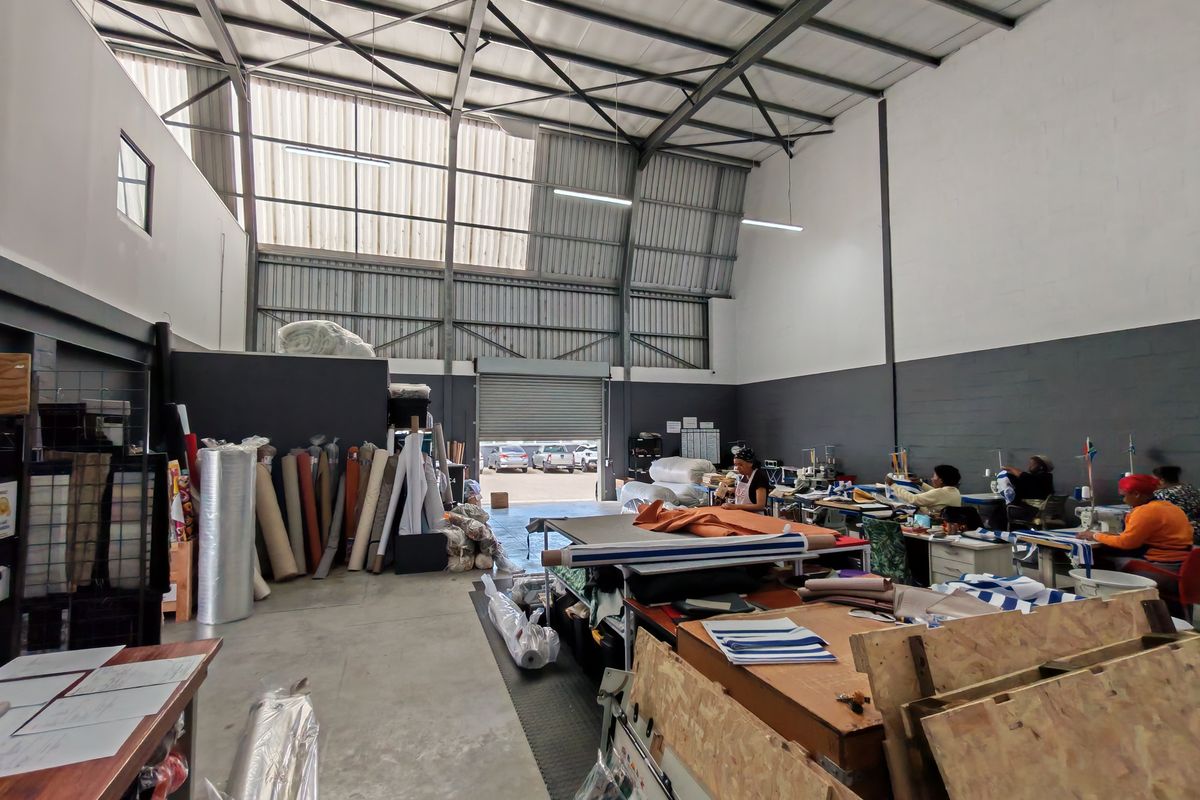 Spacious industrial warehouse unit featuring high ceilings with exposed steel trusses, concrete flooring, and a large roller shutter door for vehicle access.