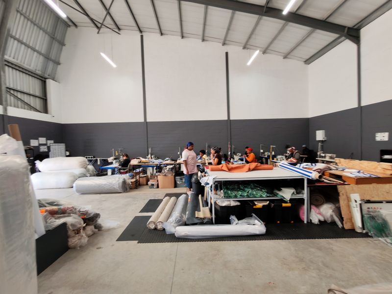 Spacious industrial warehouse unit featuring high ceilings with exposed steel trusses, concrete flooring, and functional high-bay lighting, suitable for manufacturing or storage operations.