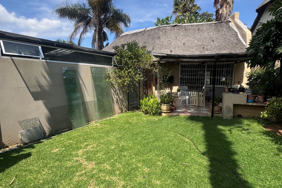 Rear garden area featuring a covered patio with a built-in braai and a traditional thatched roof structure.