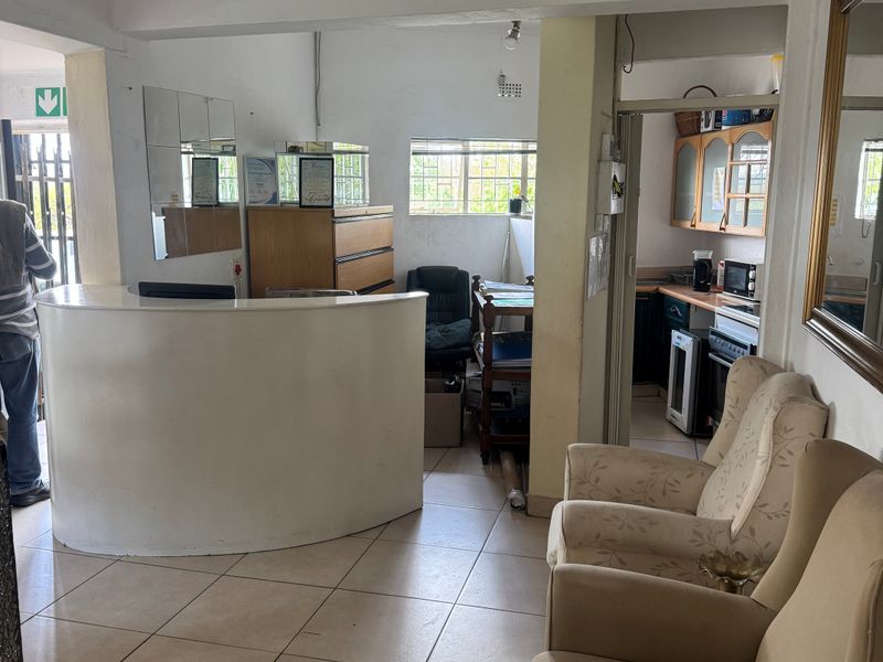 Open plan commercial reception area featuring a built-in desk, tiled flooring, and an adjacent kitchenette area.