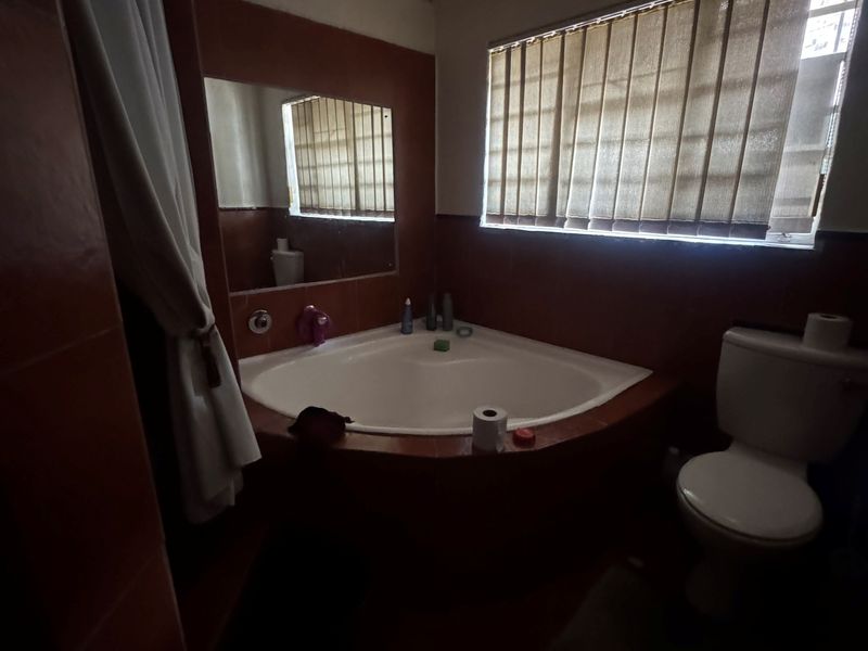 A dated bathroom featuring a corner bathtub, toilet, and tiled walls. The space requires maintenance, including repairs to the ceiling and general cosmetic updates.
