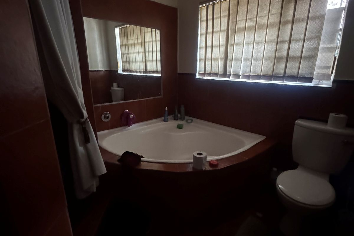 A dated bathroom featuring a corner bathtub, toilet, and tiled walls. The space requires maintenance, including repairs to the ceiling and general cosmetic updates.