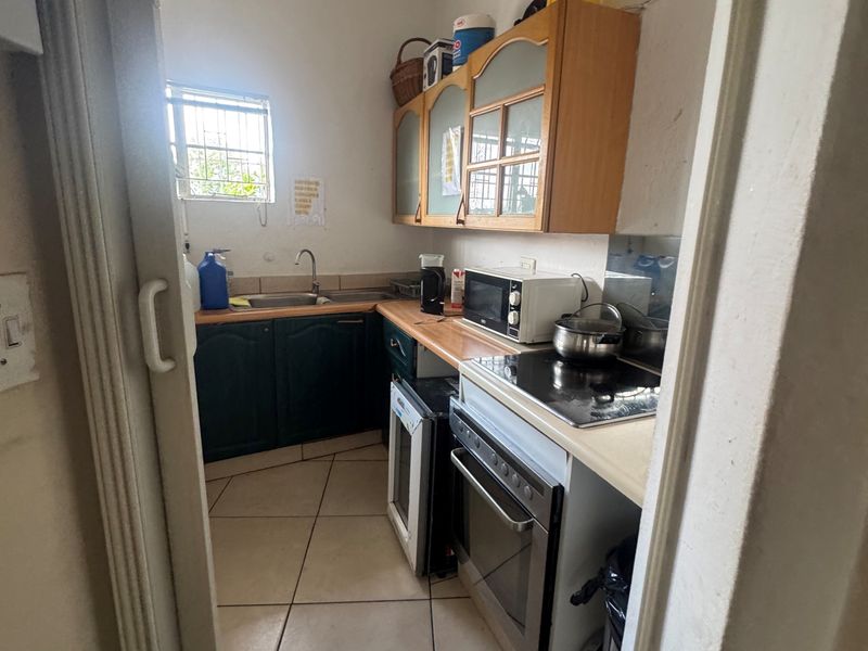 A compact scullery area featuring built-in cabinetry, laminate countertops, a stainless steel sink, and integrated cooking appliances with tiled flooring.