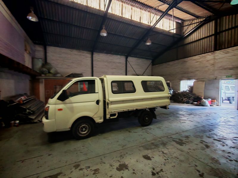 Spacious industrial utility area featuring high exposed steel roof trusses, painted brick walls, and durable concrete flooring, suitable for storage or workshop use.