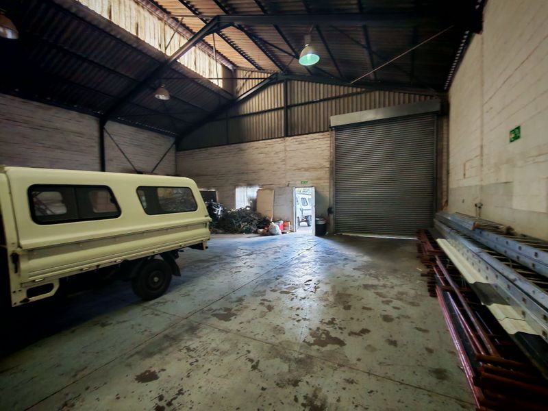 Spacious industrial utility area featuring high ceilings with exposed steel trusses, a large roller shutter door, and durable concrete flooring.
