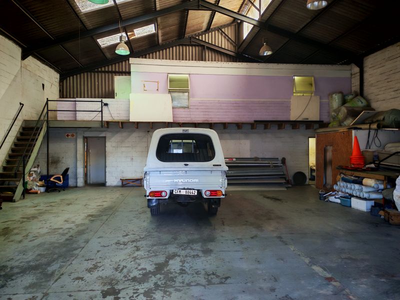 Spacious industrial garage featuring a mezzanine level, exposed steel roof trusses, and concrete flooring, suitable for workshop or storage use.
