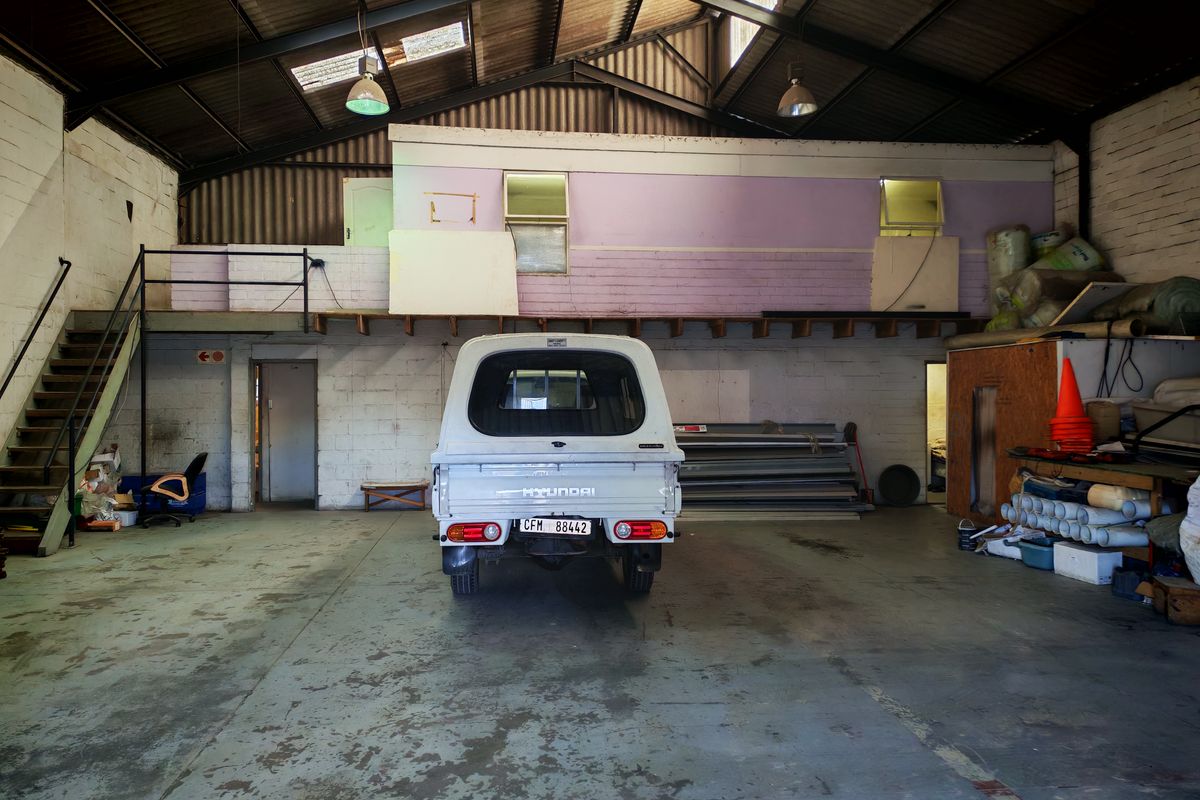 Spacious industrial garage featuring a mezzanine level, exposed steel roof trusses, and concrete flooring, suitable for workshop or storage use.