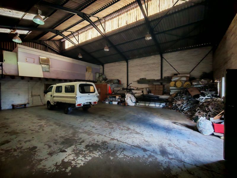Spacious industrial warehouse or garage featuring high ceilings with exposed steel trusses, clerestory windows, a mezzanine level, and durable concrete flooring.